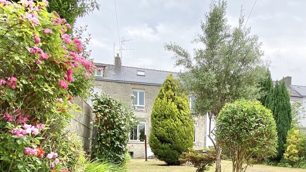 Een tuin bij een woning, met diverse planten en een huis op de achtergrond.