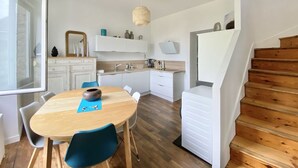 Een moderne keuken met witte kasten, een houten eettafel en een trap.