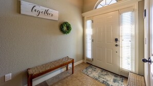 A hallway with a bench, a door, a wall-mounted sign, and a wreath. - Peaceful 3BR Base • Close to NWA Events & Trails. Secure Garage and Jetted Tub. (Pea Ridge)