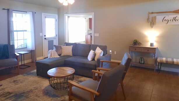 A living room with a sectional sofa, a round coffee table, and a ceiling fan. - Peaceful 3BR Base • Close to NWA Events & Trails. Secure Garage and Jetted Tub. (Pea Ridge)