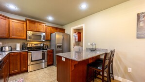 A kitchen with wooden cabinets, stainless steel appliances, a granite countertop, and a small island with bar stools. - Peaceful 3BR Base • Close to NWA Events & Trails. Secure Garage and Jetted Tub. (Pea Ridge)