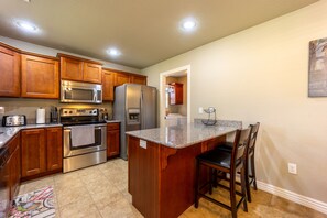 A kitchen with wooden cabinets, stainless steel appliances, a granite countertop, and a small island with bar stools.