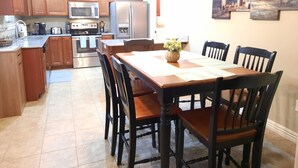 A kitchen with wooden cabinets, stainless steel appliances, and a dining area with a table and chairs. - Peaceful 3BR Base • Close to NWA Events & Trails. Secure Garage and Jetted Tub. (Pea Ridge)