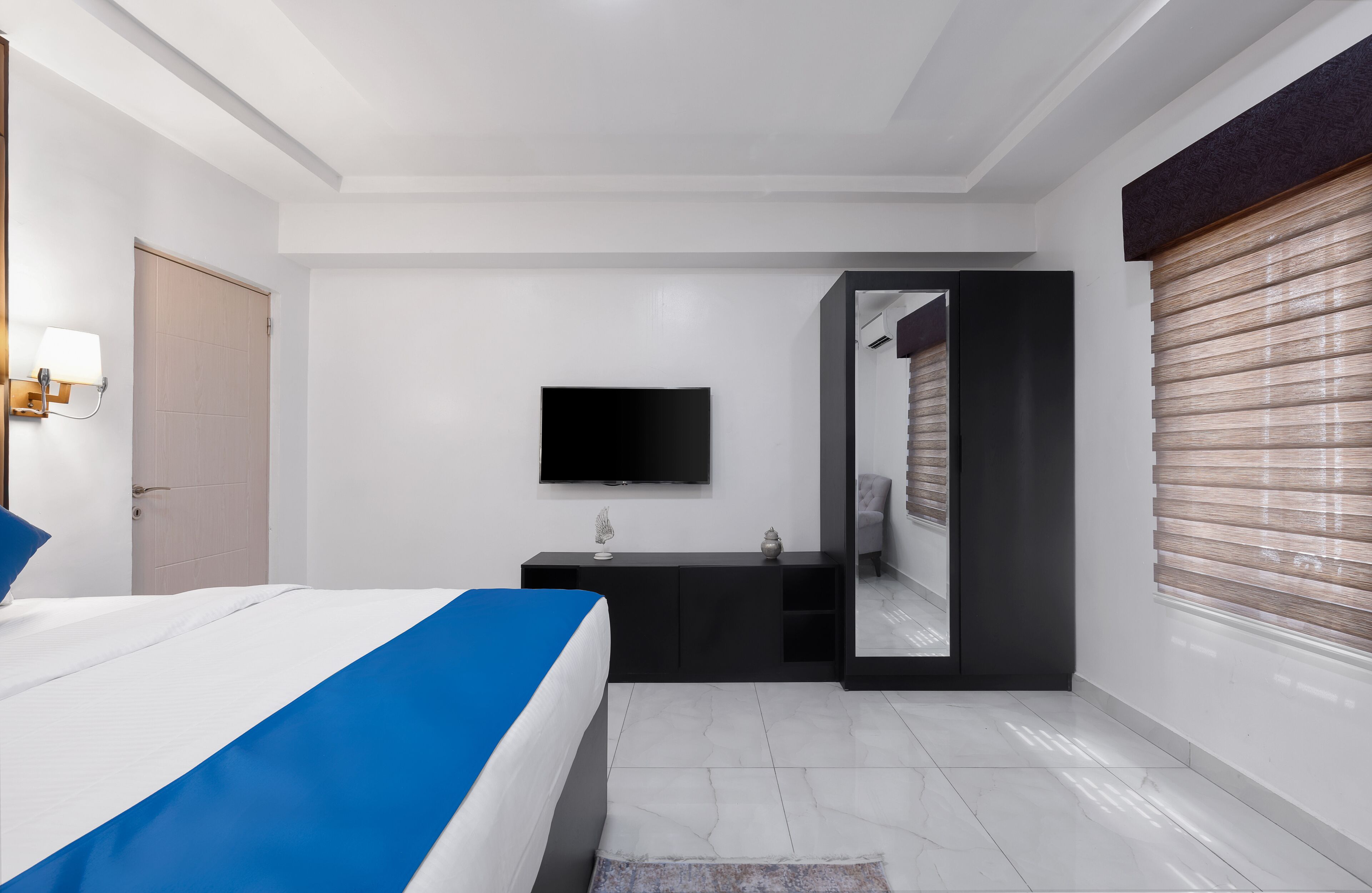 Une chambre moderne avec un lit, une télévision, une armoire et une salle de bain visible à travers une porte ouverte.