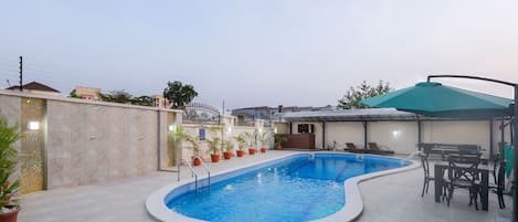A swimming pool with a tiled deck, surrounded by potted plants and outdoor furniture.