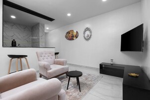 A modern living room with a large mirror, two armchairs, a coffee table, a TV, and a decorative clock.