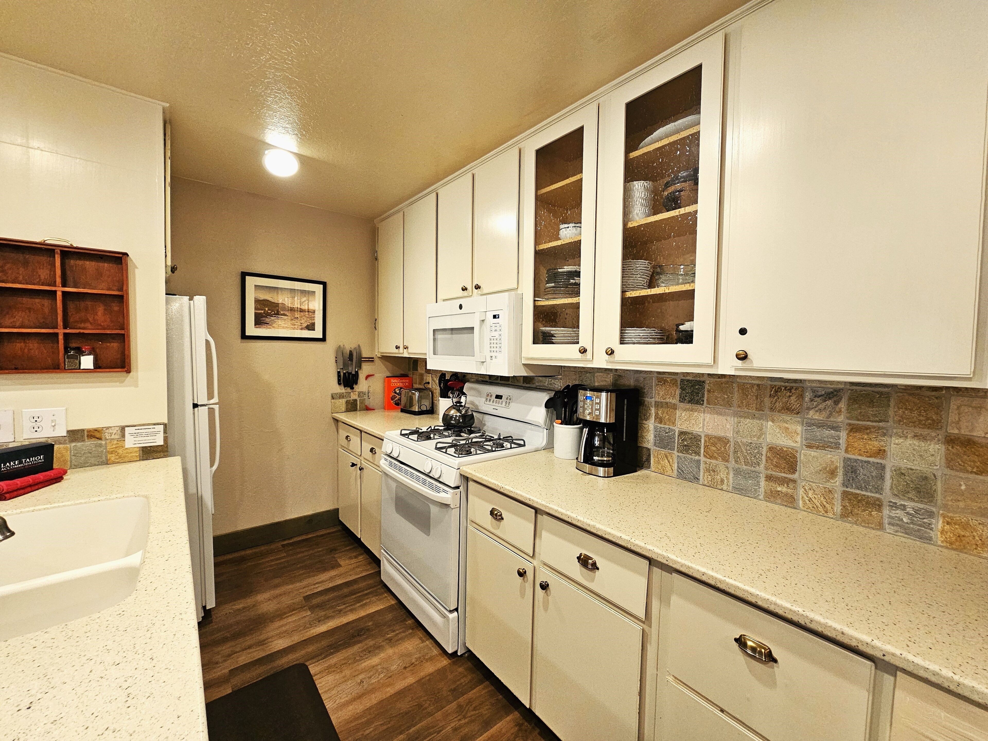 A compact kitchen with white cabinets, a microwave, a stove, and a coffee maker.