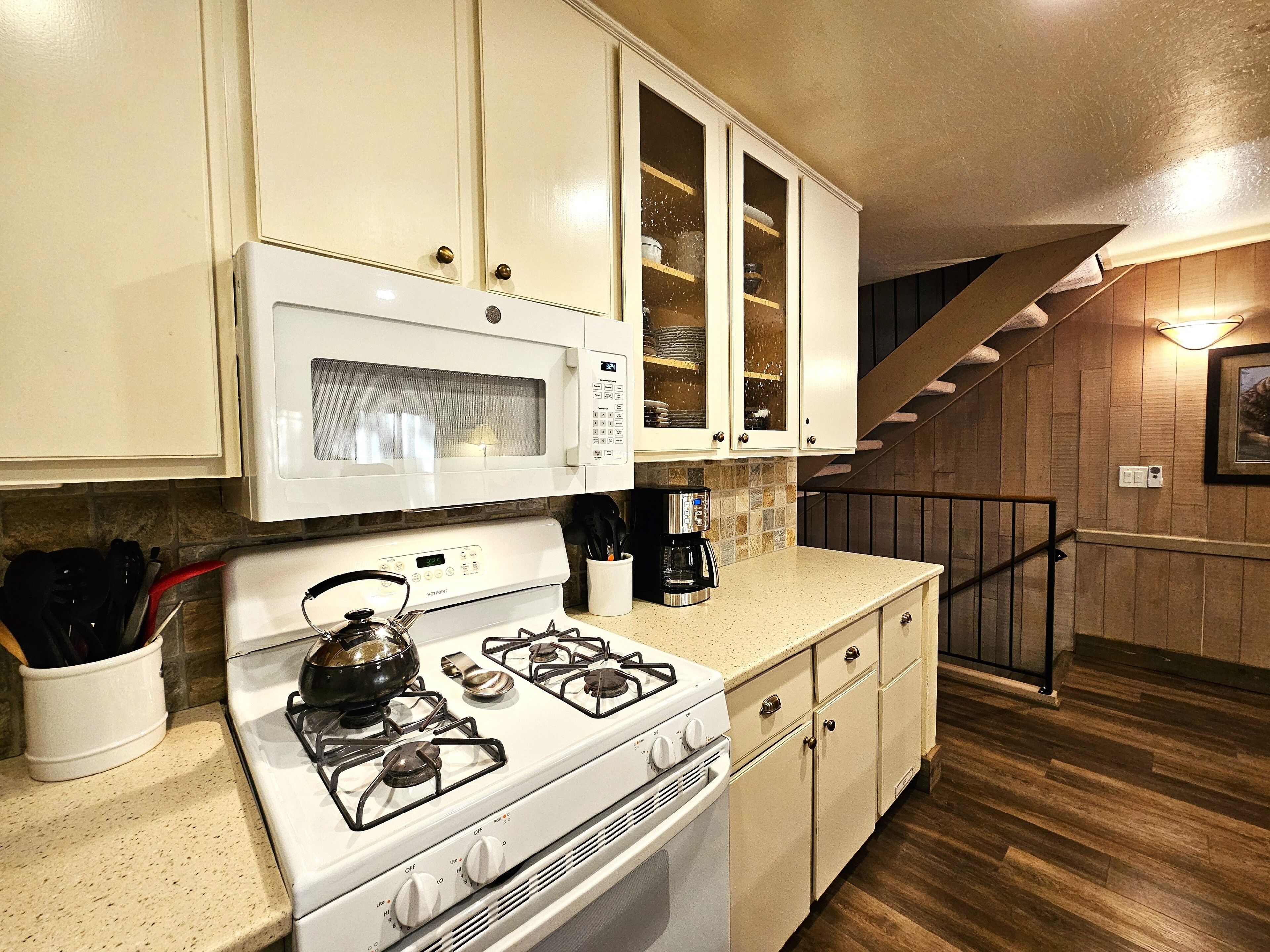 A kitchen with white cabinets, a microwave, a stove, and a coffee maker.
