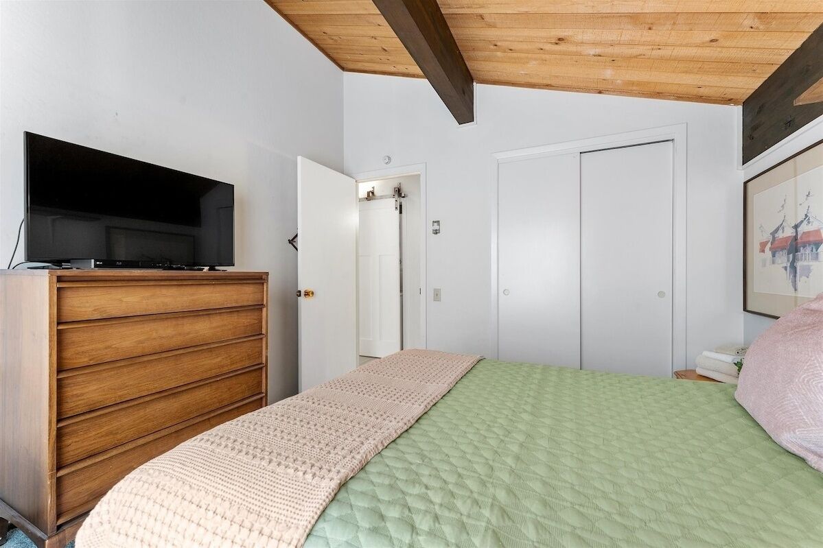 Un dormitorio con una cama, un aparador de madera, un televisor y una puerta.