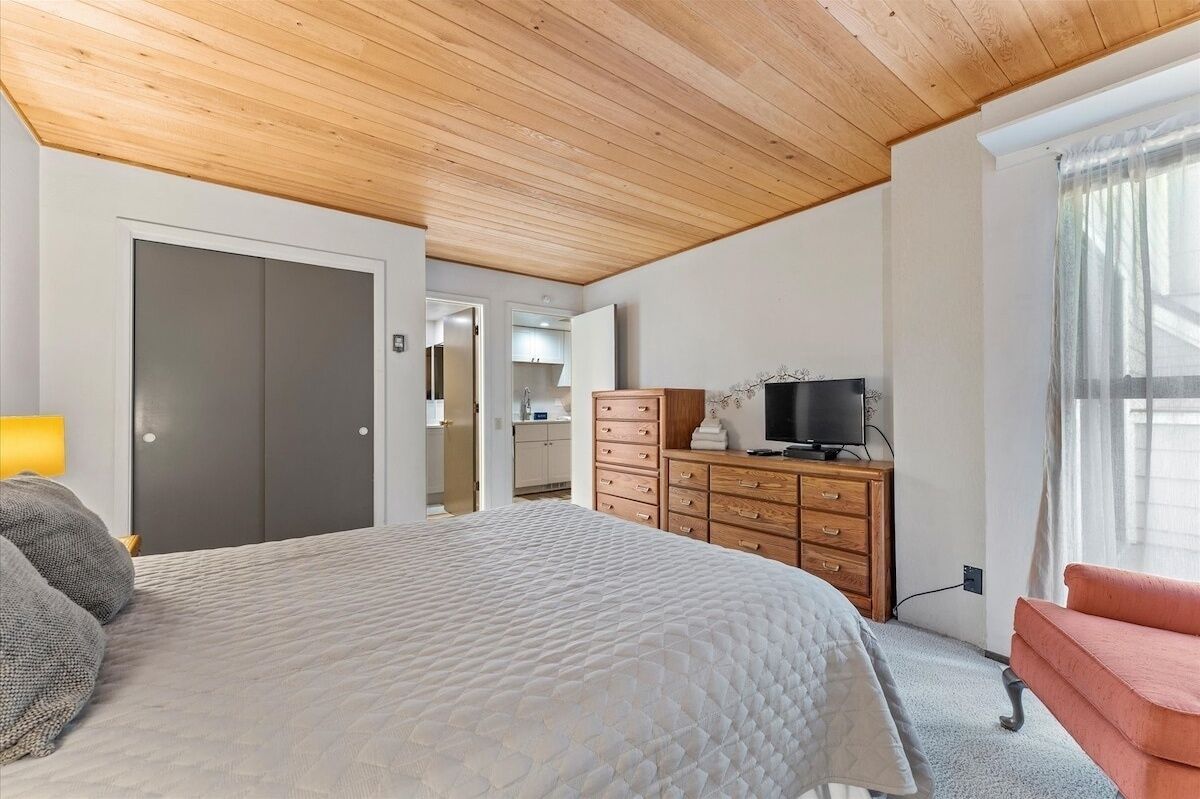 Un dormitorio con cama, cómoda, televisor y ventana con cortinas.
