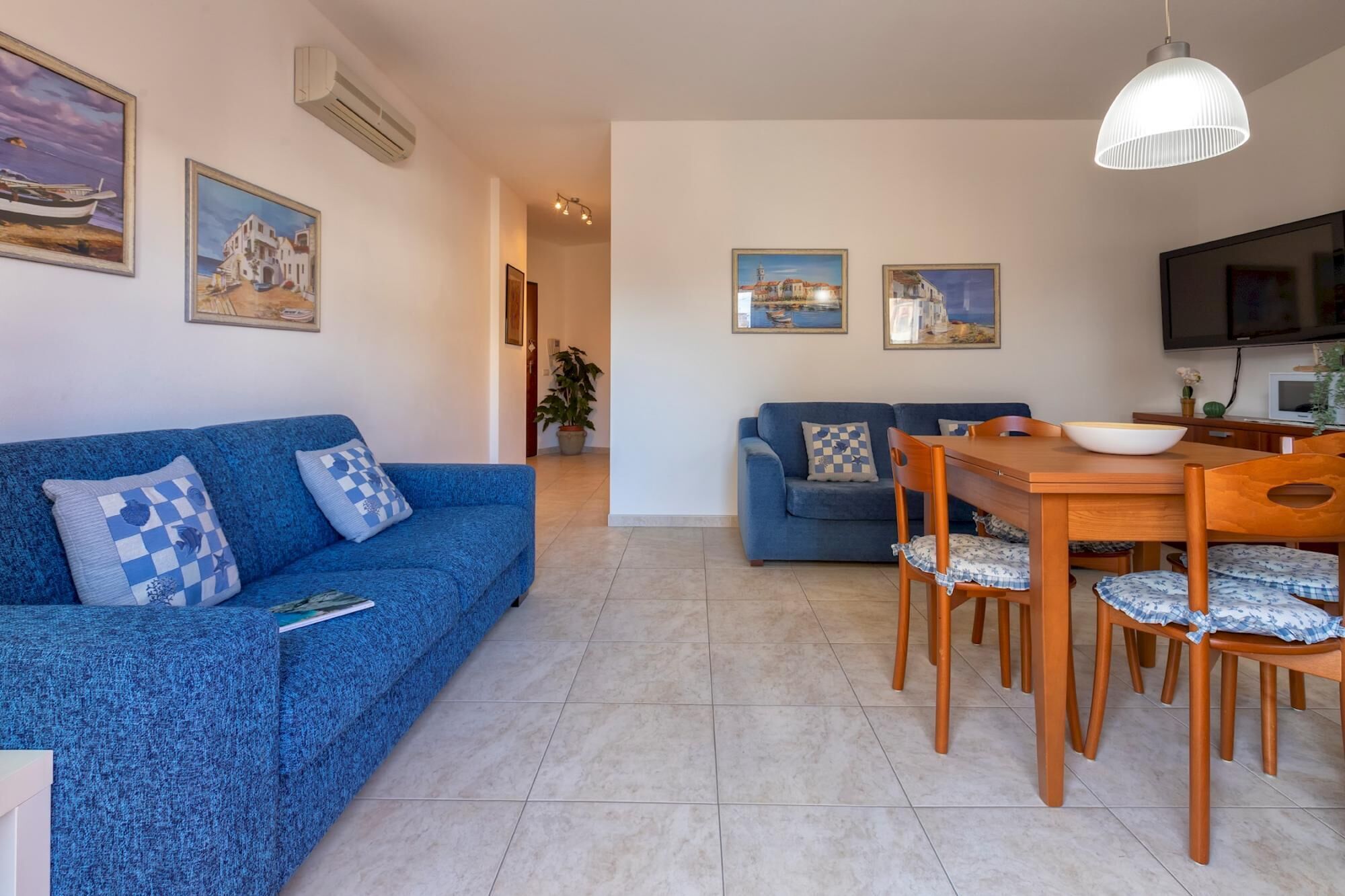 A living room with a blue sofa, a dining table with chairs, and a TV.