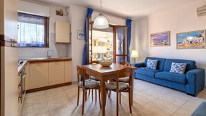A compact living space with a kitchenette, dining area, and a blue sofa. - Casa Grace in Alghero (Alghero)