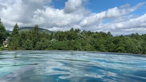 Une piscine d’eau cristalline d’un bleu éclatant, avec une vue sur une végétation luxuriante et, au loin, sur une montagne.