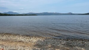 Un lac aux rives de galets, avec des montagnes lointaines se découpant sur un ciel dégagé.