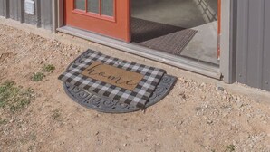 A building entrance with a red door and a checkered mat.