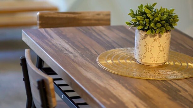 A wooden dining table with a potted plant and a woven placemat.