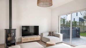 Una sala de estar moderna con televisor, sofá, otomanas y estufa de leña.