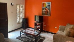 Uma sala de estar com televisão sobre um suporte, um sofá e um quadro na parede.