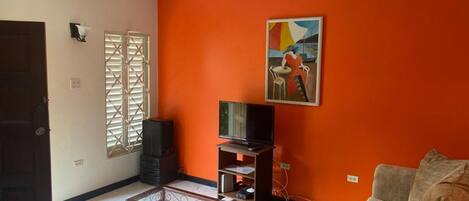 A living room with a television on a stand, a sofa, and a painting on the wall.