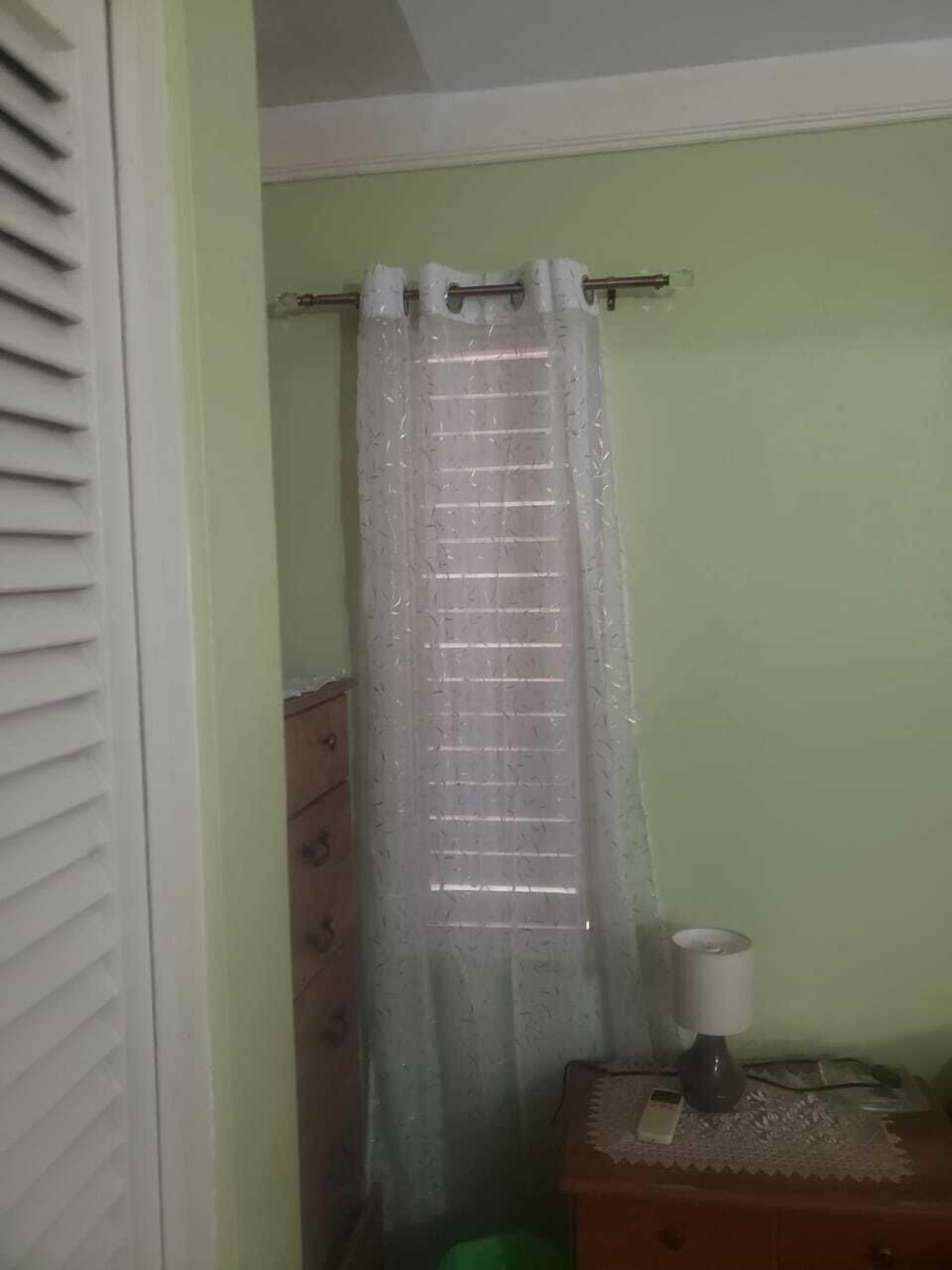 A bathroom with a shower curtain, a wooden dresser, and a lamp.