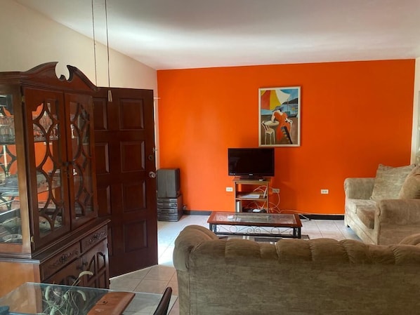 A living room with a large cabinet, a television on a stand, a sofa, and an orange wall. - Finest Accommodation Renfrew Place (Kingston)