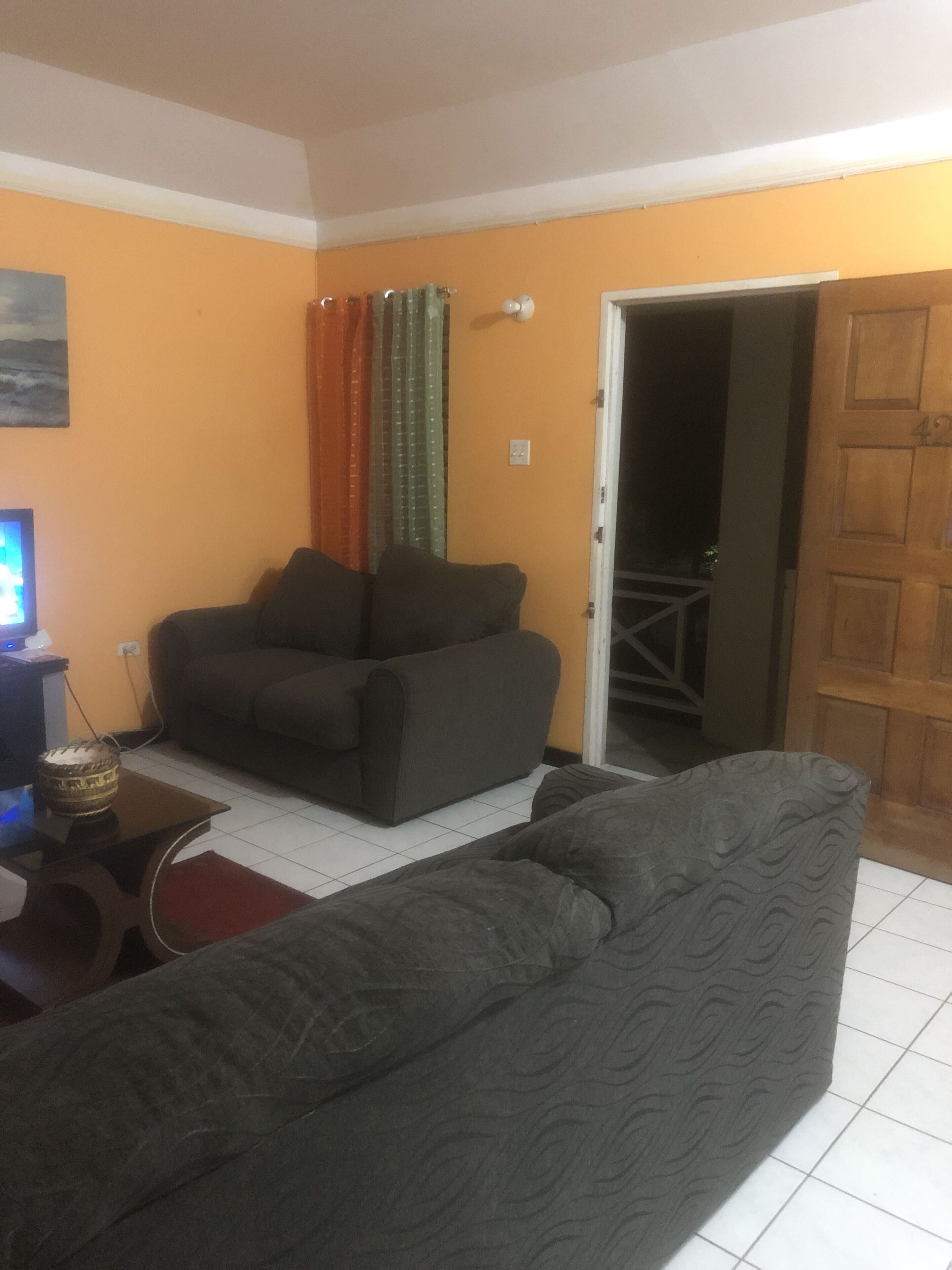 A living room with a sofa, a television, and a door leading to another room.