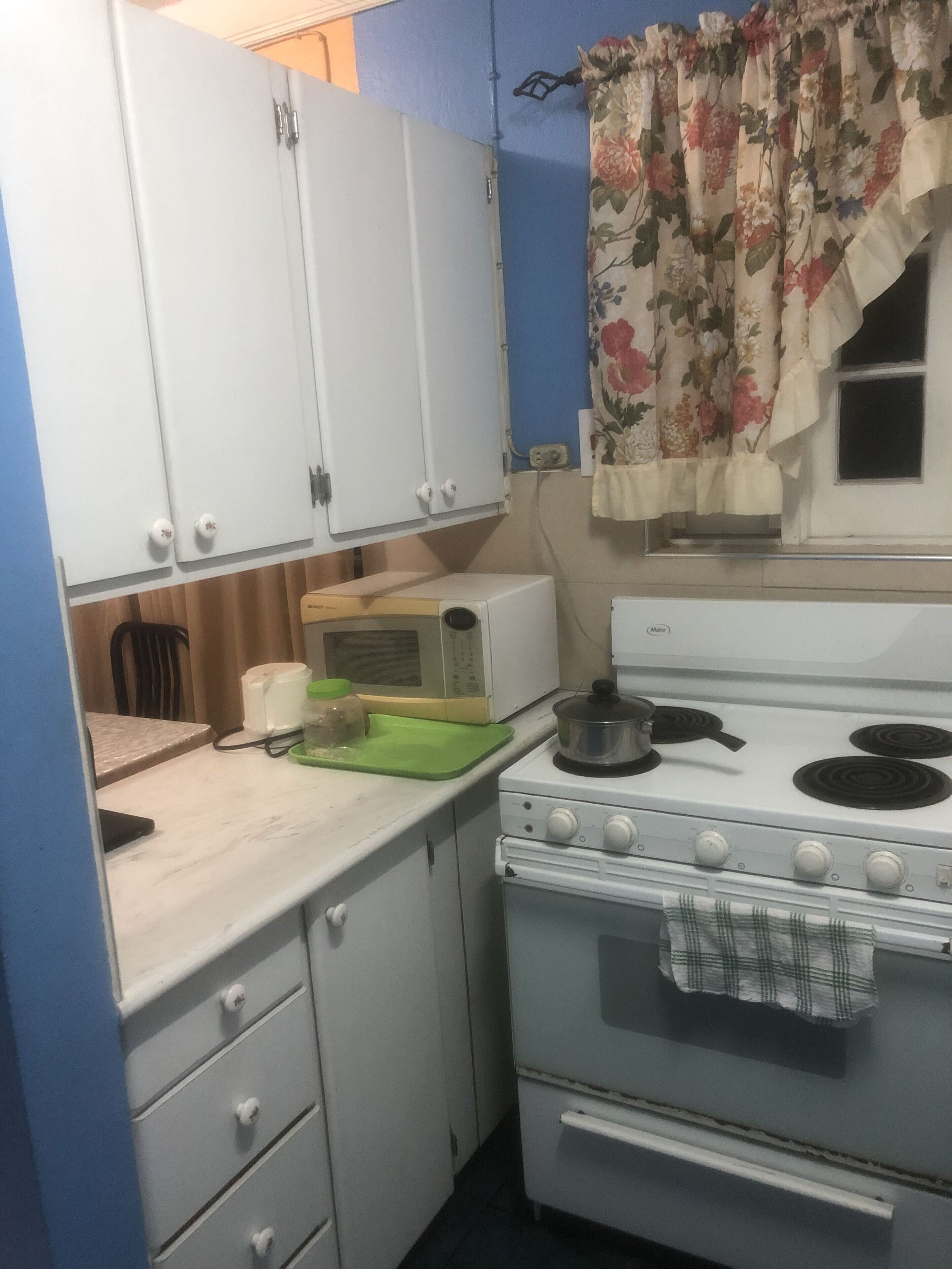 Une cuisine de taille réduite avec des meubles blancs, une cuisinière et un four à micro-ondes.