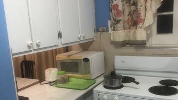 Une cuisine de taille réduite avec des meubles blancs, une cuisinière et un four à micro-ondes.