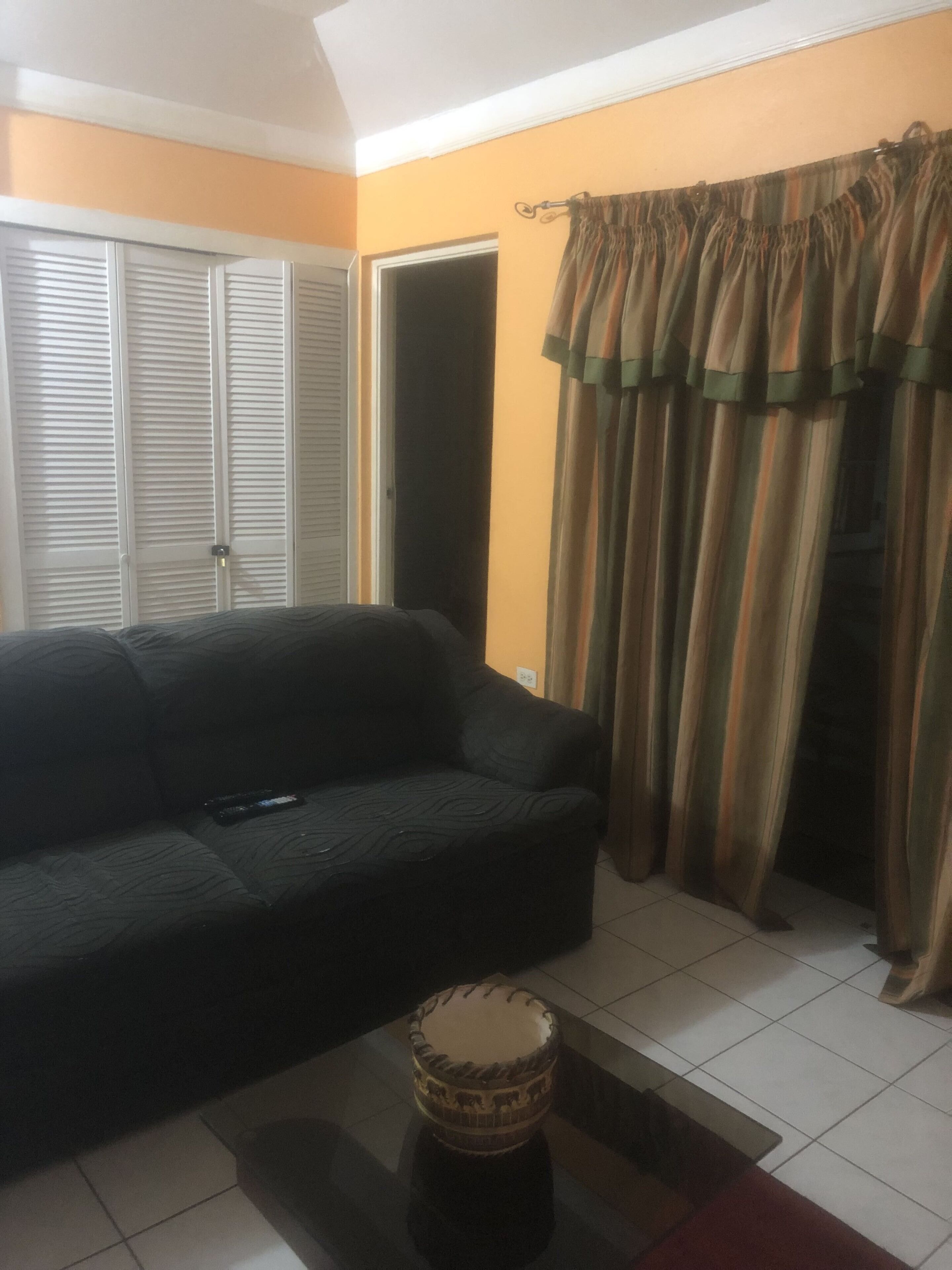 A living room with a dark sofa, a small round table, and a pair of curtains.