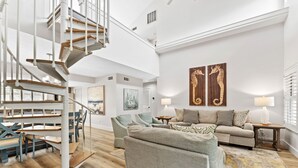 A spacious living area with a modern staircase, a comfortable sofa set, and a dining area with wooden tables and chairs. - Updated Hidden Dunes Resort Villa w/ Spacious Porch! Short walk to Beach/Pool (Miramar Beach)