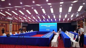 A conference room with a long table, a stage with a screen, and a camera on a tripod.