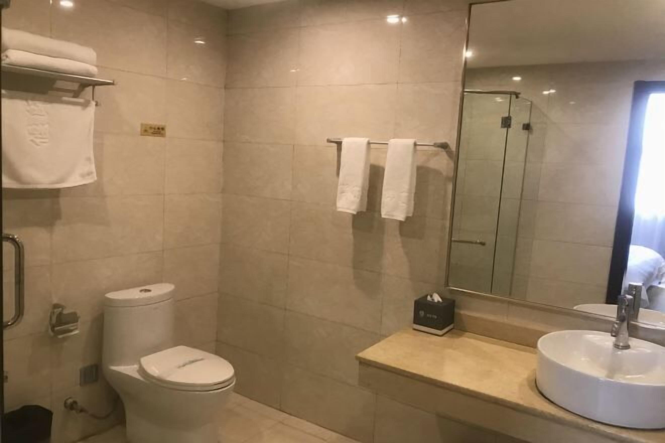 A bathroom with a toilet, sink, and mirror. There are towels hanging on a rack and a glass shower door.