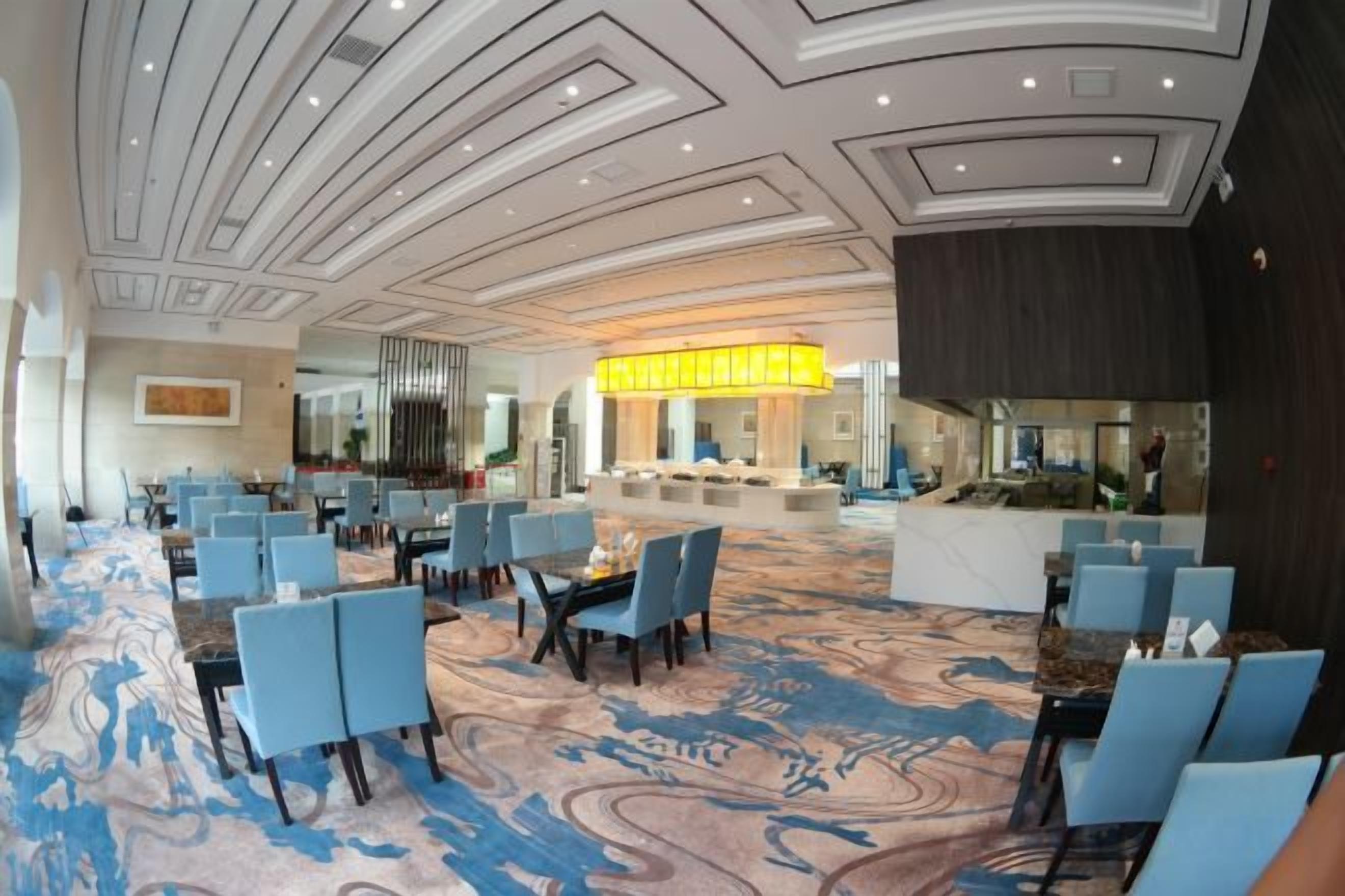 A hotel lobby with a marble reception desk, blue seating area, and a patterned carpet.
