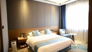 Habitación de hotel con una cama grande, mesitas de noche, una silla, una mesita pequeña y un ventanal con cortinas.
