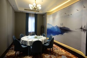 Un salón de conferencias con una mesa redonda, sillas, una araña y un mural en la pared.