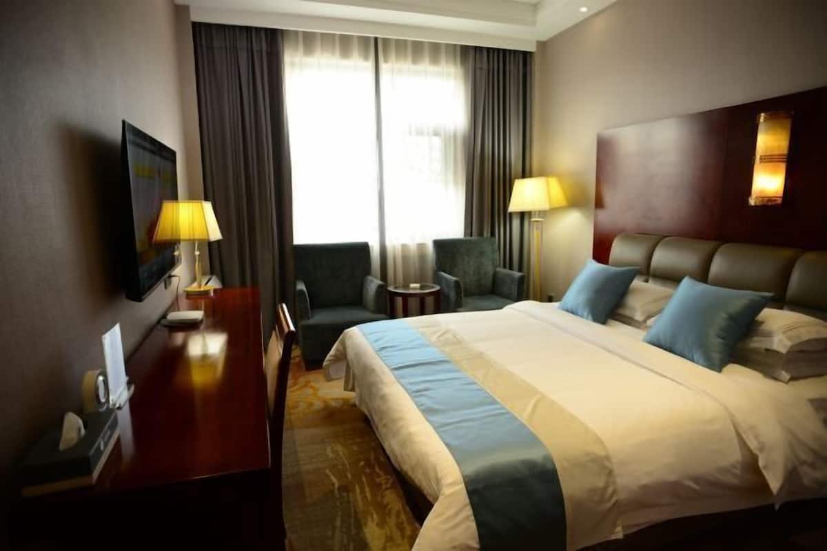 Una habitación de hotel con una cama grande, dos sillones, un escritorio y un televisor.
