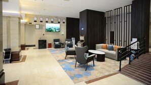 Un vestíbulo espacioso con diseño moderno, que incluye una zona de estar con sofás y sillones, un televisor de pantalla plana en la pared y una escalera que conduce a un nivel superior.
