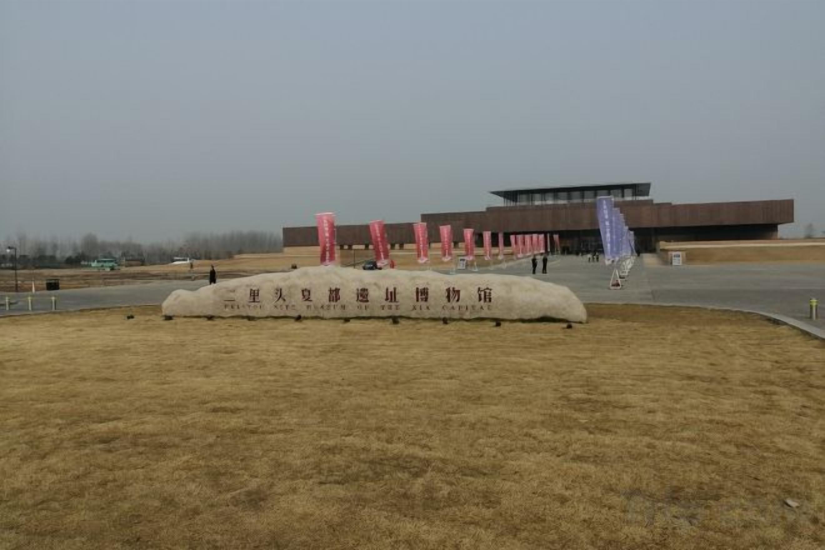 A building with a modern architectural style, a grassy area with a stone monument, and a clear sky.