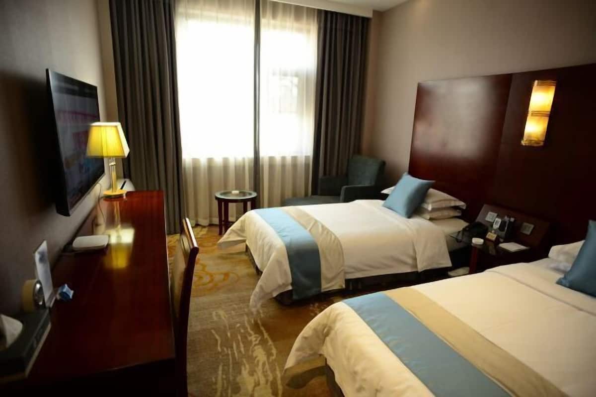 Habitación de hotel con dos camas, un escritorio, una silla, un televisor y vistas al exterior.