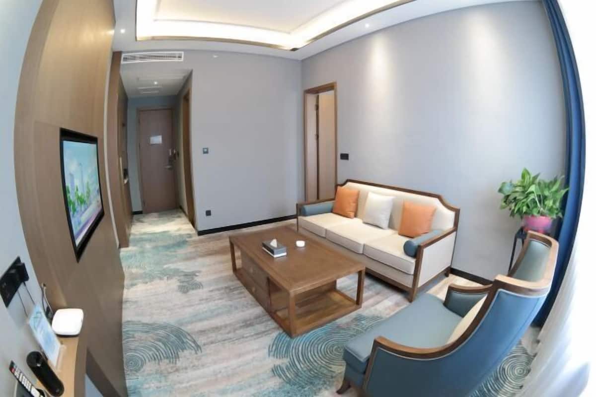 Una sala de estar moderna con un sofá, una mesita de centro y una silla. Hay un televisor en la pared y una planta en la esquina.