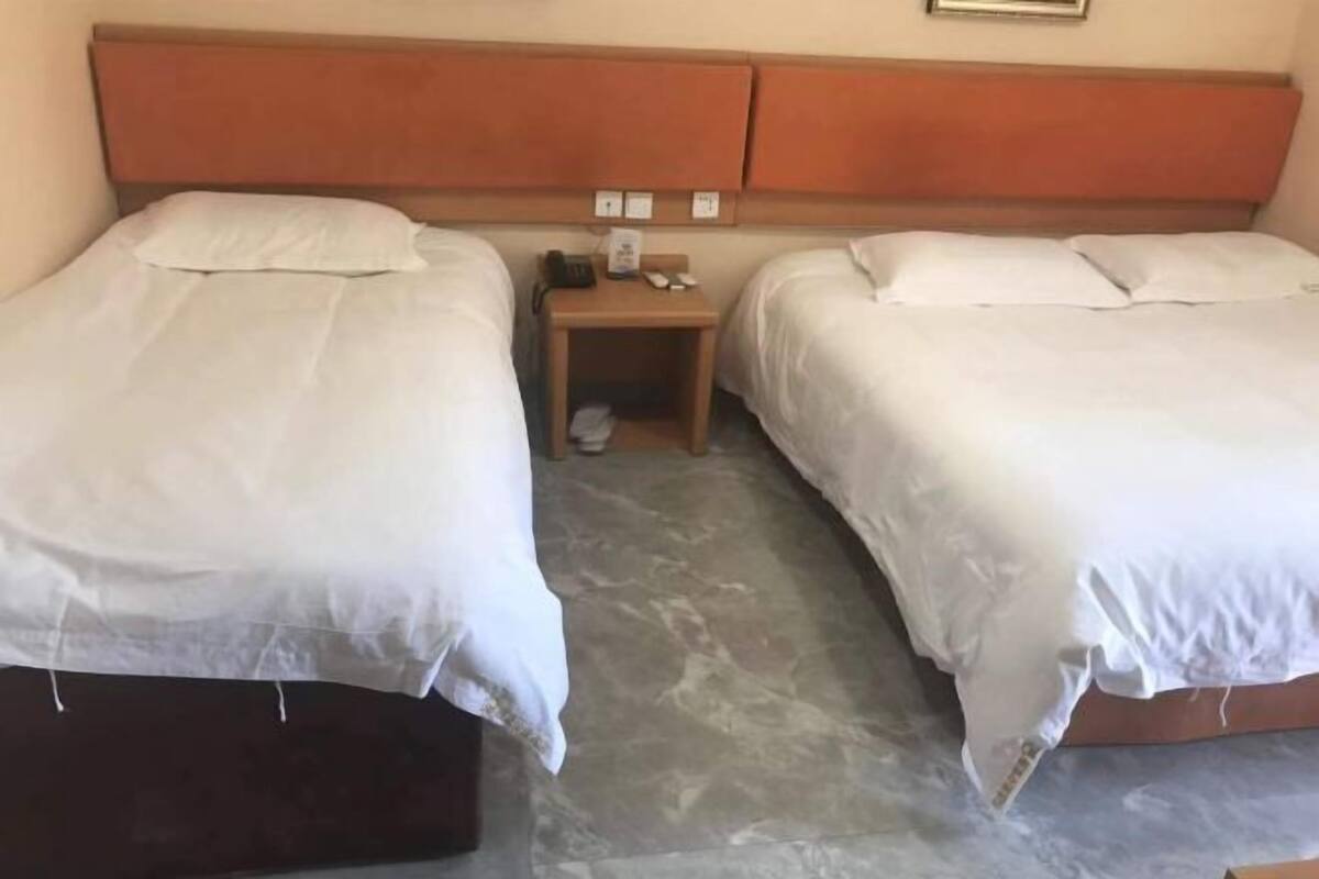 A hotel room with two single beds, a wooden nightstand with a phone and a small table, and a marble floor.