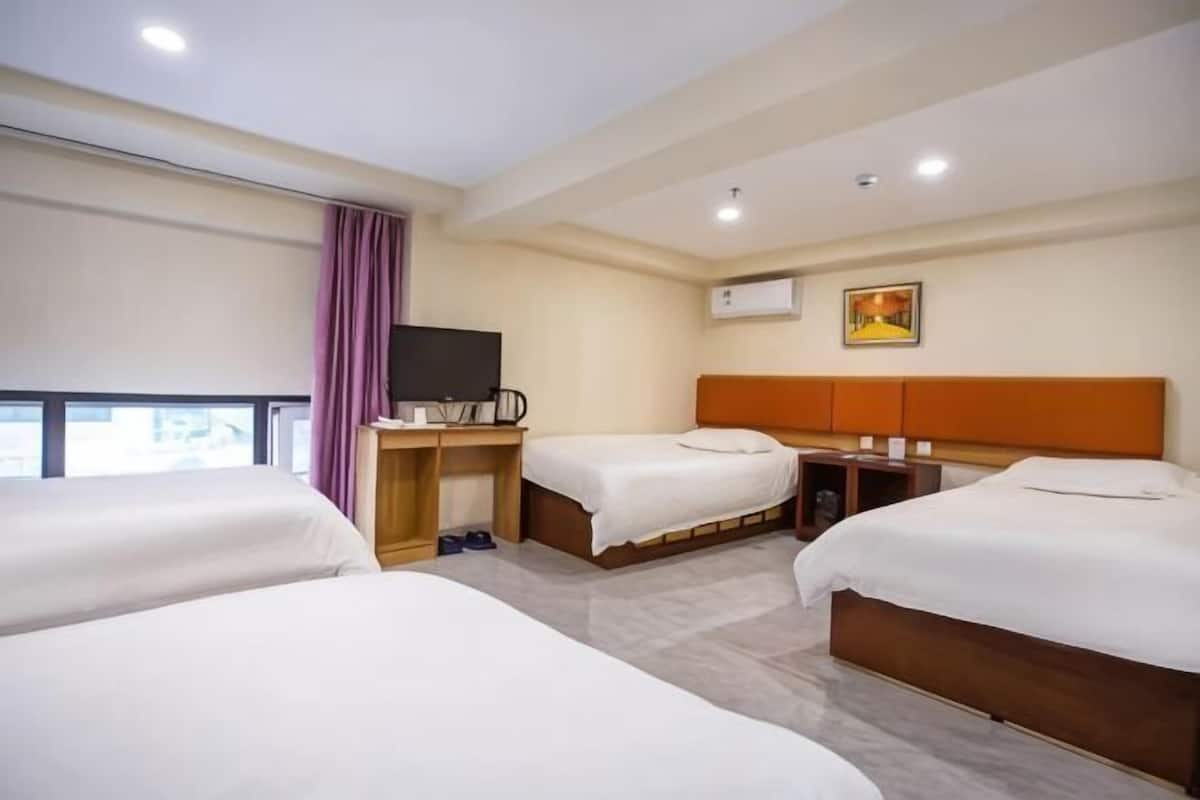A hotel room with two beds, a desk, a television, and a window with curtains.