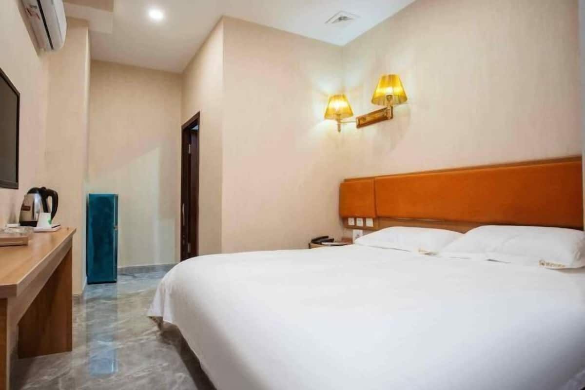 A hotel room with a bed, bedside lamps, a desk with a kettle, and a blue chair.