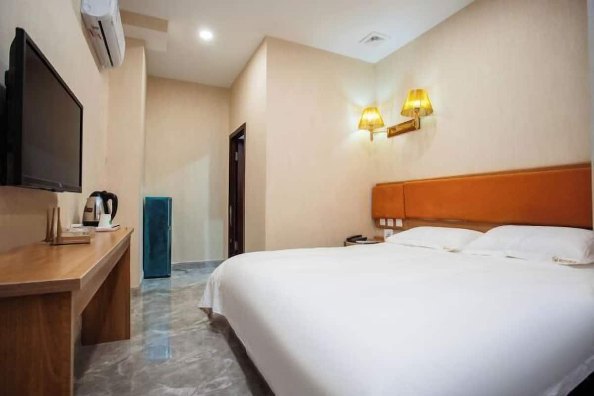 A hotel room with a bed, bedside table, lamp, and a television.