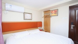 Ett hotellrum med en säng, ett sängbord, en luftkonditioneringsanläggning, en garderob i trä och en dörr.