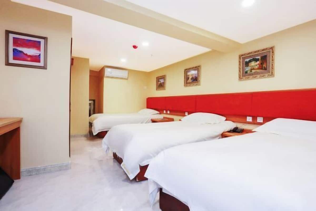 A hotel room with three beds, a wooden desk, and a red headboard.