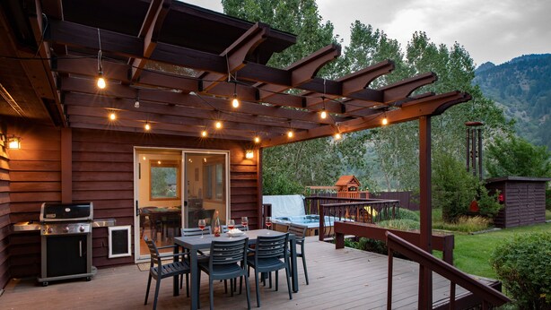 Une terrasse en bois avec une pergola, un espace salon extérieur et un barbecue.