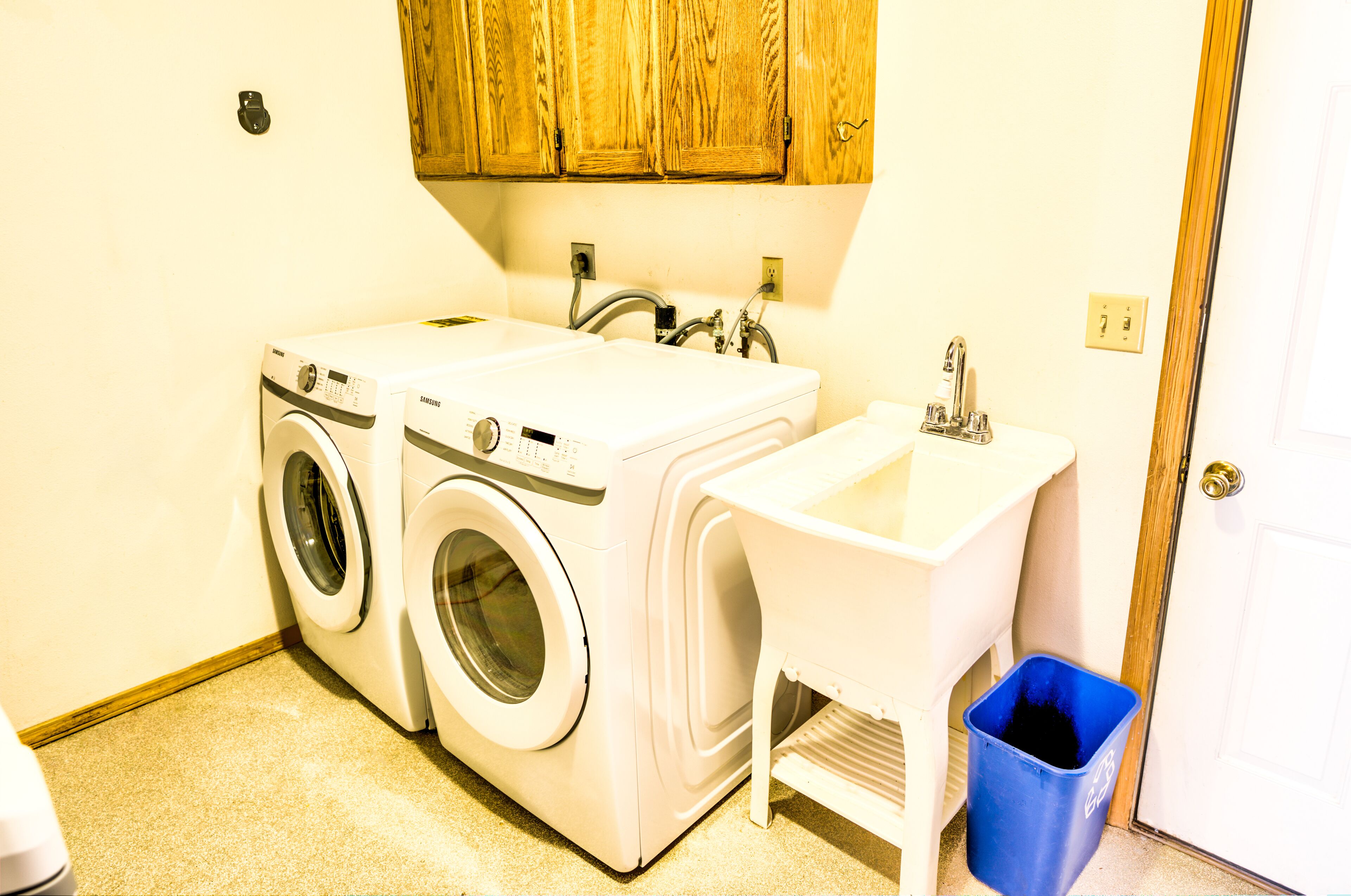 Un área de lavandería con dos lavadoras, un lavabo y un cubo de basura azul.