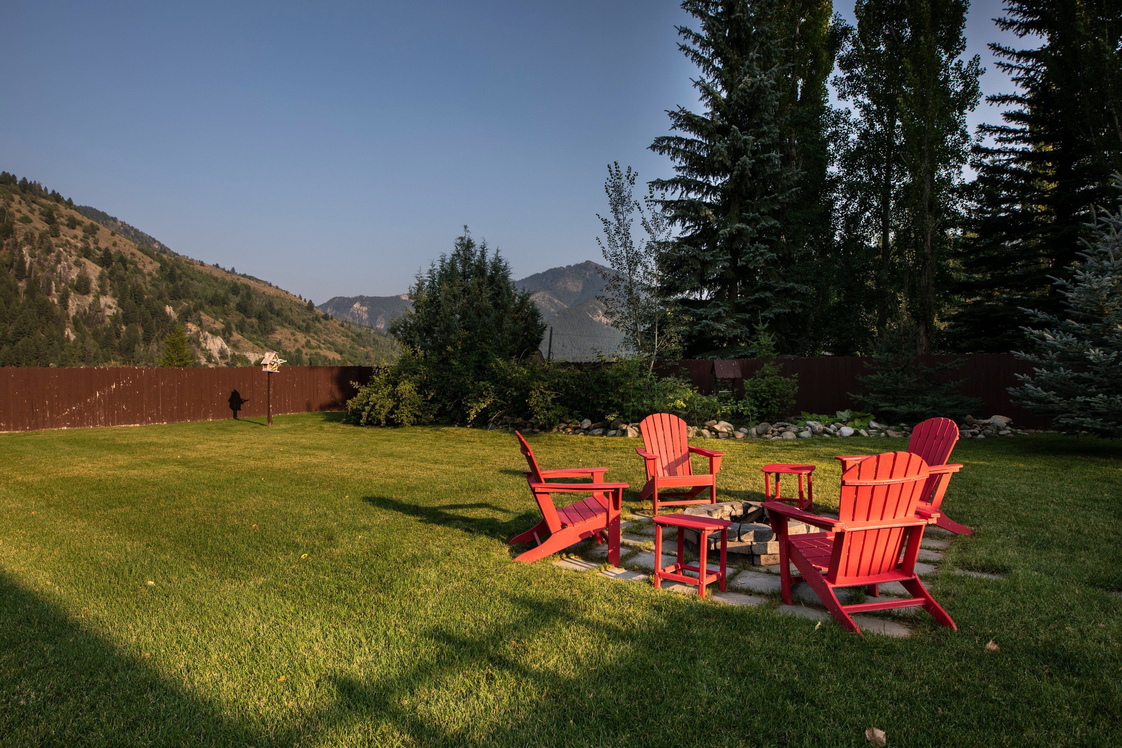 A backyard with a red Adirondack chair set, a small table, and a stone pathway.