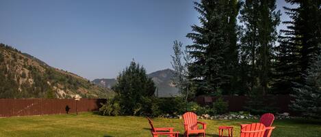 A backyard with a red Adirondack chair set, a small table, and a stone pathway.